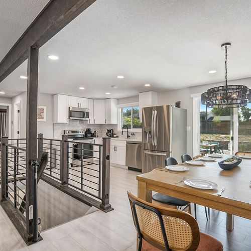 Bright and stylish open floor plan connecting the living room, dining area, and kitchen, with a chic staircase leading to the lower level.