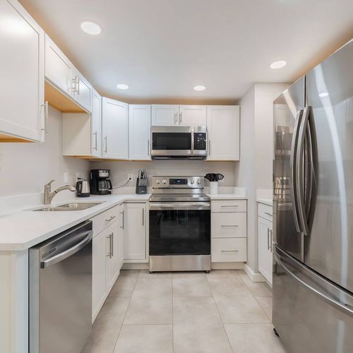 - fully equipped kitchen with white cabinetry, stainless appliances, and sleek countertops
- compact layout includes a full size fridge, microwave, dishwasher, and coffee essentials
- neutral palette and tile floors make cleanup quick and easy