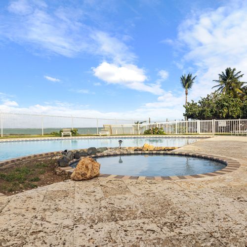 Tome el sol junto a nuestra serena piscina, rodeada de un exuberante paisaje tropical y una vista del cielo azul claro.