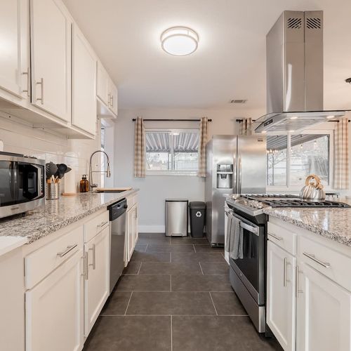 - modern kitchen featuring granite countertops, sleek cabinetry, & a gas cooktop
- fully equipped with stainless appliances, essentials, & a large sink with a pull down faucet
- natural light & checkered curtains add charm to this highly functional s