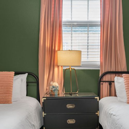 Warm-lit bedroom w/ a bed, sage walls & flowing peach curtains for a calm night in.
