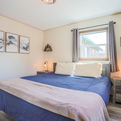 - unwind in a plush bed dressed in deep navy tones and soft neutral accents
- wake to natural light streaming through the window beside cozy bedside lighting
- minimalist mountain artwork and warm wood floors create a peaceful retreat