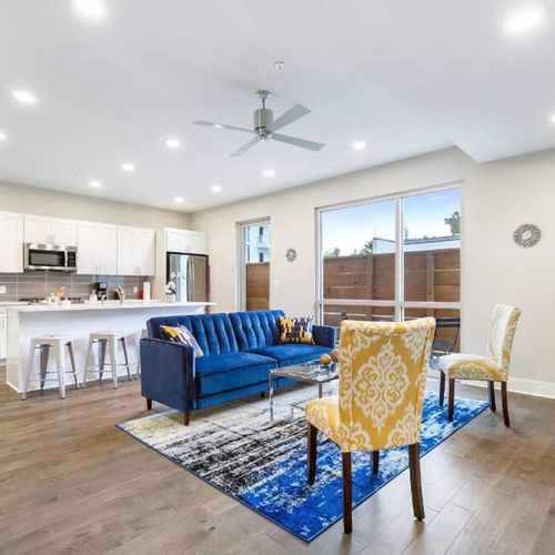 Airy living room w/ ceiling fan, blue sofa & dining nook bathed in natural light.