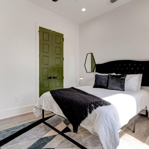 Bedroom w/ bold dark headboard, crisp white linens & a dramatic green door.