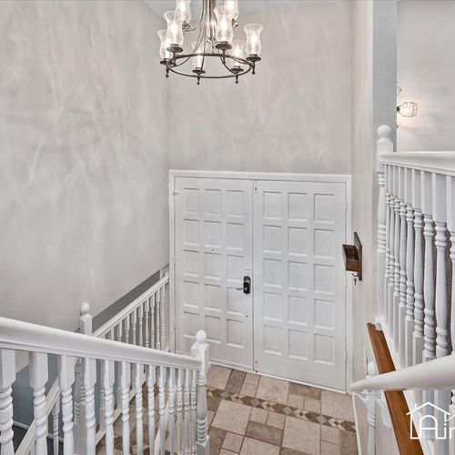 - elegant entry with double white paneled doors and decorative light fixture above
- tiled landing and split stair design create a grand first impression on arrival
- bright white railings and neutral walls keep the space airy and welcoming