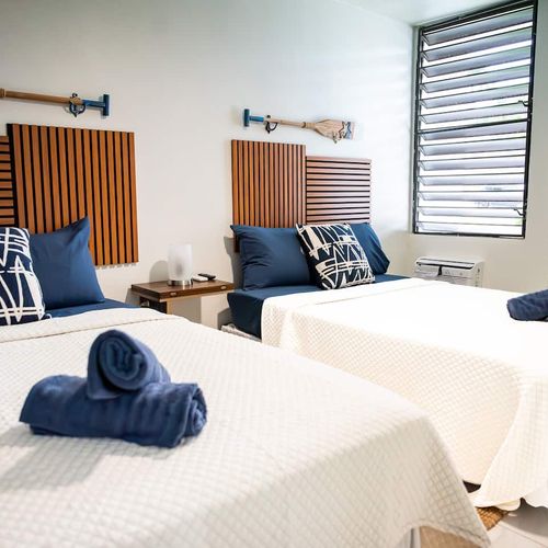 Perfect for friends or family, this comfortable room features two cozy beds, each with stylish wooden headboards and nautical-inspired decor.