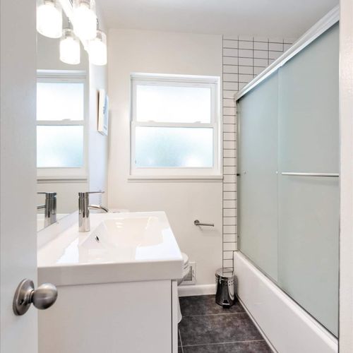- bright and clean bathroom with large vanity, modern lighting, and tile detail
- frosted glass window and shower doors ensure natural light and privacy
- simple yet stylish with black tile floors and sleek chrome fixtures