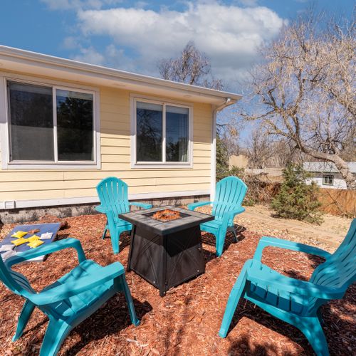 The house exterior is bathed in sunshine, surrounded by lush trees and a perfect outdoor seating area.