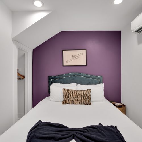 Bedroom 1 w/ a plush bed framed by a deep purple wall & soft, layered bedding.