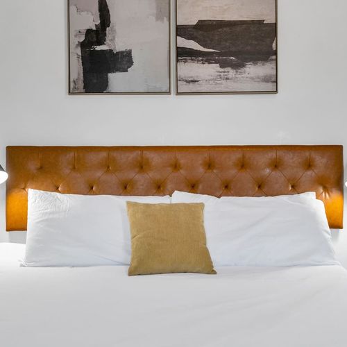 Close-up of a tufted orange headboard w/ layered pillows for a luxe, boutique feel.