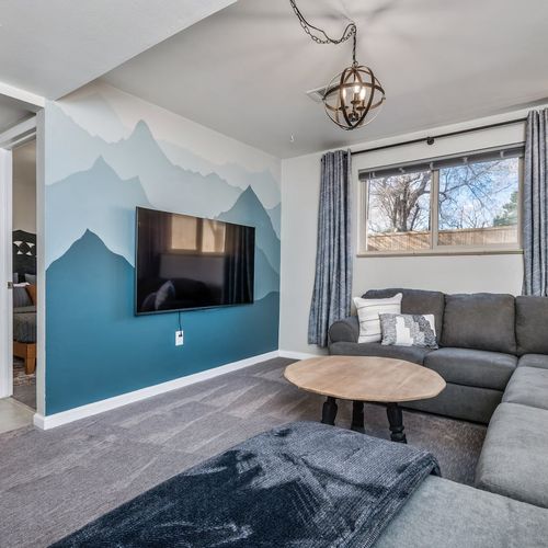 - unique mountain mural frames the flat screen tv in this cozy bonus lounge
- plush gray sectional and soft carpet invite movie nights or casual naps
- ideal for families needing extra space to gather unwind and recharge