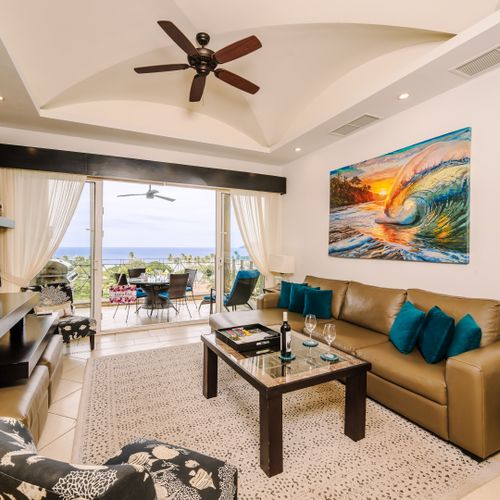 Open-concept living and dining with leather sectional, ocean-view sliders, and covered balcony with dining beyond.