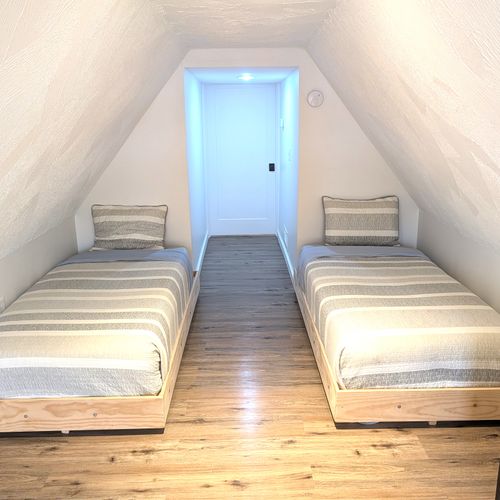 BEDROOM #3 (UPPER LEVEL):  Large and long upper bedroom with a queen-size bed, 2 twin beds, dresser, nightstands, and lamps.