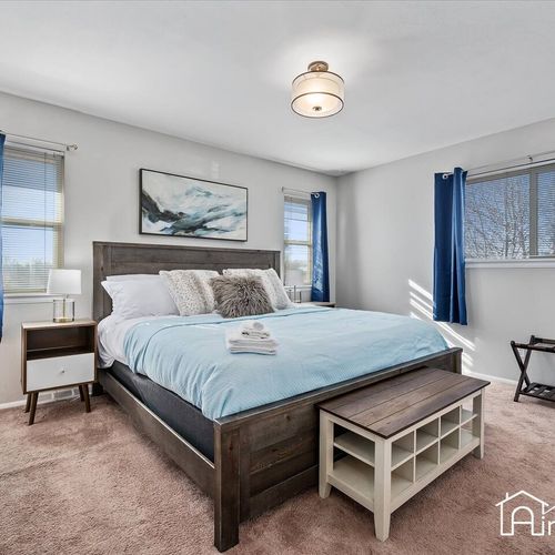 - restful king bedroom with deep blue bedding, rustic wood bed frame, & soft carpeting
- windows on two sides fill the space with daylight while blackout curtains offer rest
- modern bedside tables & bench seating add style & convenience to your stay