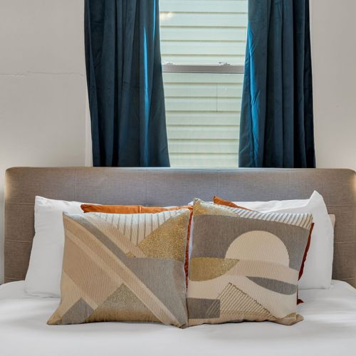 Bed w/ warm, layered pillows in earthy tones for a relaxed, welcoming vibe.
