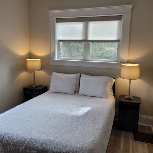 Bedroom #1 (main floor):  features a queen-size bed, ceiling fan, window a/c unit, nightstands, lamps, chair, dresser, mirror, and a closet.