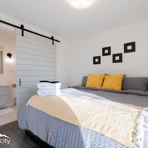 - bright and inviting bedroom with a king sized bed dressed in cozy gray and gold tones
- modern barn door opens to a sleek ensuite bathroom with stylish lighting
- towels and essentials thoughtfully prepared for a comfortable, restful stay