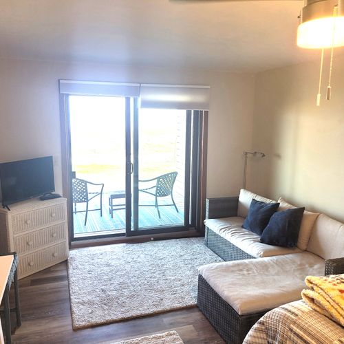 BEDROOM #1 (PRIMARY):  Features a queen-size bed, sofa bed, lakeview, private ensuite bathroom, private entrance from the back patio, private television, nightstand, lamp, ceiling fan, dresser, and shelves