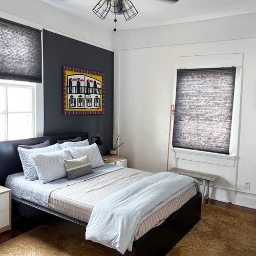 Restful bedroom w/ neatly made bed & natural light streaming through the windows.