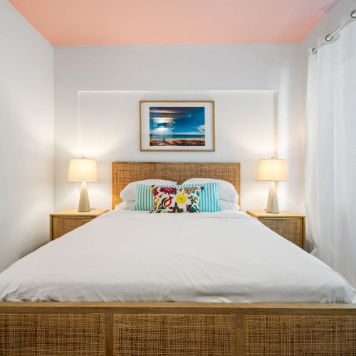 Dreamy Tropical Retreat: Unwind in our inviting bedroom featuring a comfortable bed with a stylish rattan headboard, flanked by warm, ambient lighting. The vibrant wall art adds a touch of paradise.