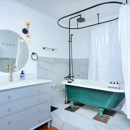 - standout bathroom with deep green clawfoot tub and rainfall shower combo
- marble style tile walls, brass fixtures, and round mirror blend modern with vintage
- floating vanity and ambient lighting elevate the overall spa like vibe