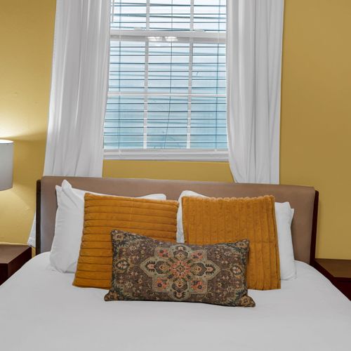 Warm bedroom w/ mustard & white pillows layered for comfort & style.