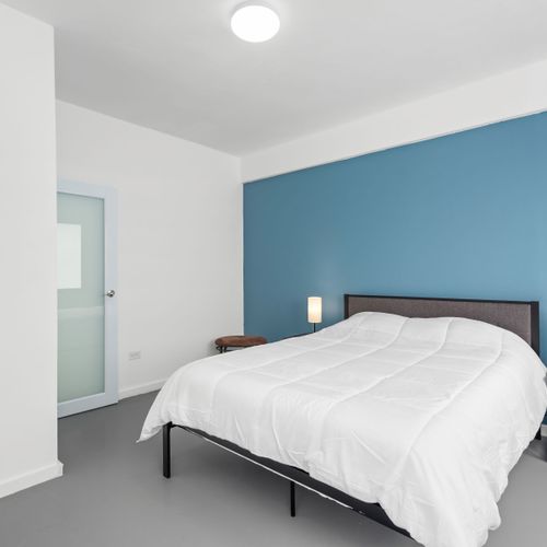 A serene space boasting a plush bed, minimalist decor, and a vibrant blue accent wall that adds a touch of warmth and sophistication.