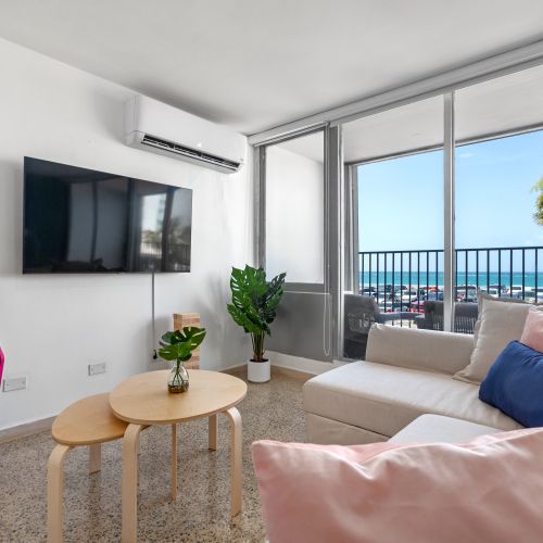 Bright living room with ocean view balcony, flat-screen TV, comfortable seating, and arcade game for entertainment.