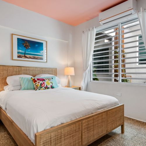 Coastal Comfort: Drift off to sleep surrounded by tasteful design, including a natural wood bed frame and a stunning piece of art that evokes sunny beach days. Perfect for recharging after a day of exploration.