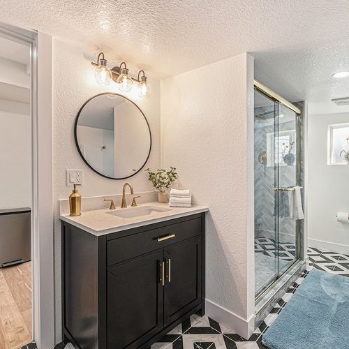 - step into a bold, modern bathroom with striking black and white tile floors and sleek gold accents
- vanity area includes a round mirror, soft lighting, and a touch of greenery
- enjoy a glass walk in shower with custom tiling and bright ambiance