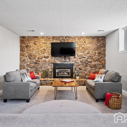 - cozy lower level lounge with dual sofas, a mounted tv, and a natural stone fireplace
- great for movie nights or winter retreats with plush carpet and ambient lighting
- wood coffee table and cheerful pops of red décor tie the whole space together