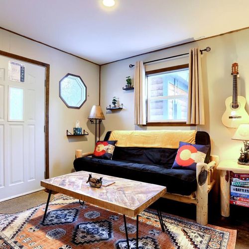 - enjoy evenings with board games stacked beside a log nightstand and soft lighting
- wall mounted guitar and decor bring personality to this cozy corner nook
- futon and vibrant rug add warmth to your relaxed mountain retreat