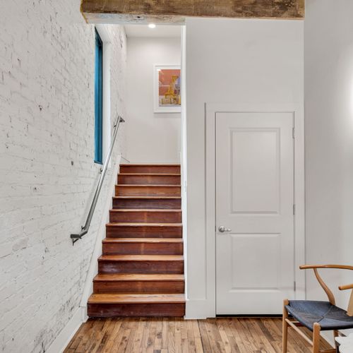 Exposed brick, warm wood tones, and modern touches—this inviting stairway leads to your cozy New Orleans retreat.