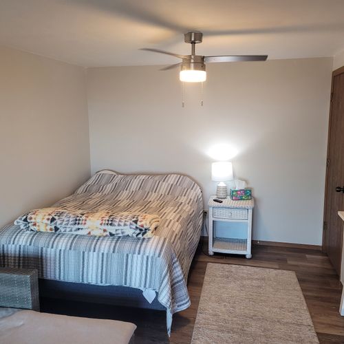 BEDROOM #1 (PRIMARY):  Features a queen-size bed, sofa bed, lakeview, private ensuite bathroom, private entrance from the back patio, private television, nightstand, lamp, ceiling fan, dresser, and shelves