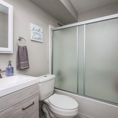 - light wood vanity and soft gray palette create a calming minimalist vibe
- frosted shower doors and wall mounted towel ring provide function and ease
- subtle wall art and essentials like soap and towels are ready for use