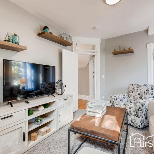 - comfy lounge area with a flat screen tv, built in shelves, and bright decor touches
- white console and floating shelves create functional style and storage
- perfect space to unwind, stream your favorites, or play games