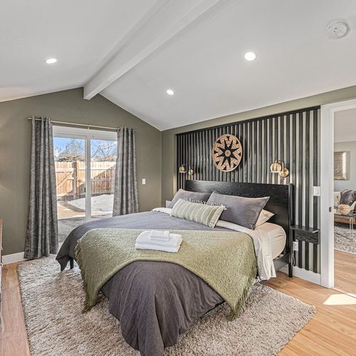 - spacious primary bedroom with king bed opens to backyard through sliding doors
- green walls and textured decor invite you into a serene and inviting space
- relax under high ceilings with plush bedding and calming natural light