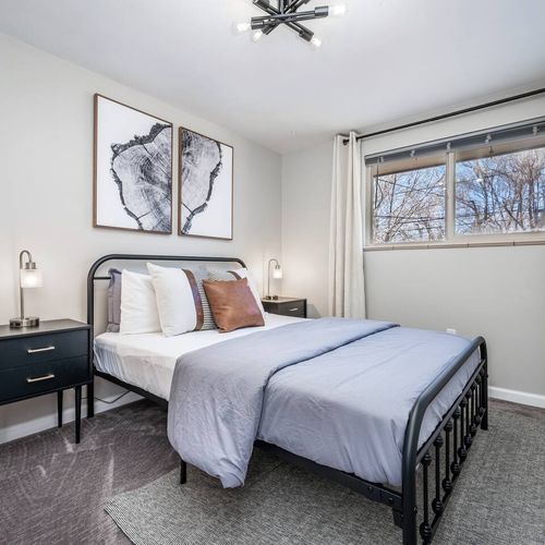 - sleek black metal bed frame paired with soft gray bedding and plush pillows
- minimalist decor including abstract prints and neutral tones throughout
- large window fills the space with light for a bright airy atmosphere
