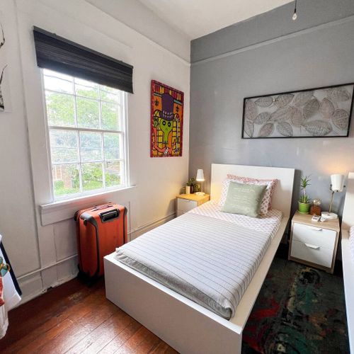 Cozy single bed tucked into a bright, compact room w/ natural light.