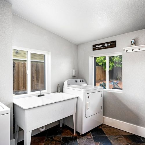 - bright laundry room with full size washer and dryer for guest convenience
- includes deep utility sink, natural light, and cheerful wall décor above
- large windows and spacious layout make everyday chores feel easy and fresh