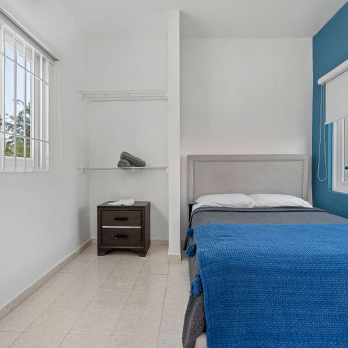 Enjoy revitalizing rest in a roomy bedroom with a lavish bed, modern aesthetics, and an energizing blue accent wall that enhances your well-being.