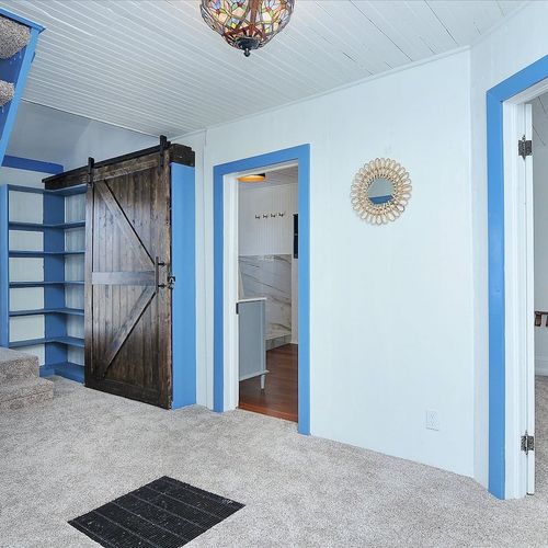 - unique entryway featuring a custom dark wood barn door and built in blue shelving
- open riser staircase leads to the cozy loft, adding architectural charm
- carpeted floors, natural light, and eclectic accents make this space warm and welcoming