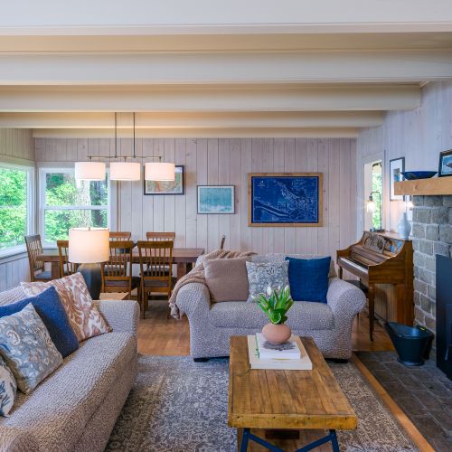 Living  and dining room share an open spacer with large windows bringing in light to a historic mantle and fireplace.