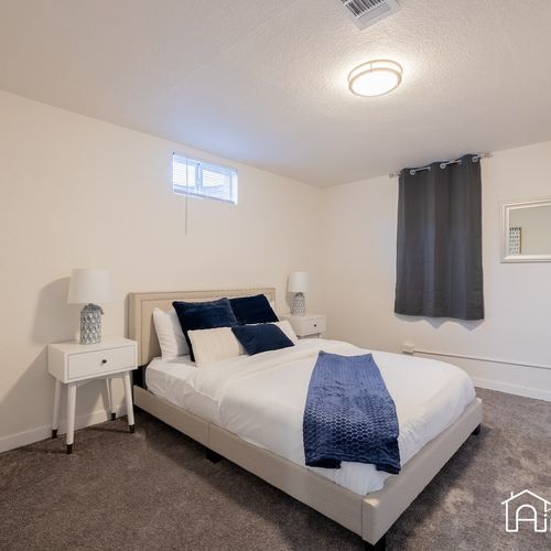 The first bedroom downstairs includes a queen size bed, black out curtains, and nightstands. Luggage racks and shelves are available for your belongings.