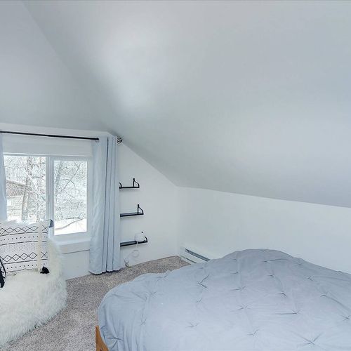 - quiet corner bedroom with soft lighting, plush bedding, and sloped ceiling design
- fuzzy accent chair with pillows makes a perfect nook for reading or lounging
- snowy views through the window enhance the calm and cozy atmosphere