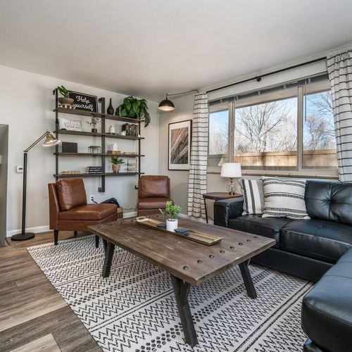 - inviting living space with black leather sectional and two warm leather chairs
- statement bookshelf styled with greenery books and unique accessories
- abundant sunlight and cozy textures make this space a true gathering zone