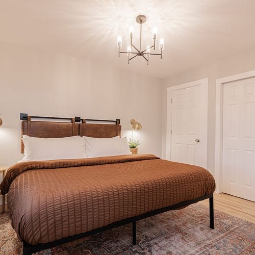 - sleep soundly in a serene bedroom with a soft brown comforter and leather accented headboard
- modern chandelier and brass reading lamps set a warm, ambient glow
- features blackout curtains, a spacious closet, and calming minimalist design