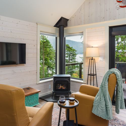 Step into a bright, minimalist space where a warm fire, soft leather chairs, and floor-to-ceiling windows bring nature right inside.