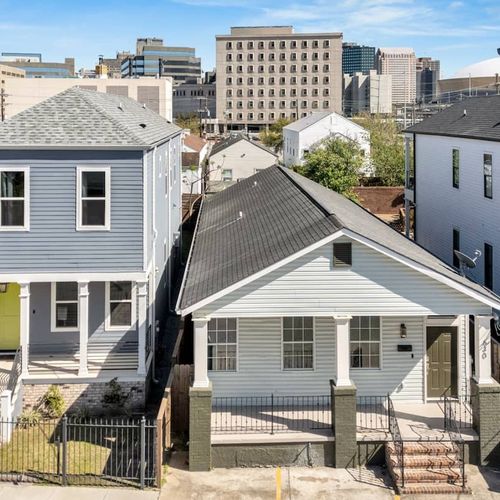 Charming exterior of the home w/ classic New Orleans architecture & green seating out front.