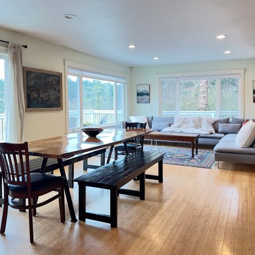 Open-concept living and dining with forest views from every window—perfect for gathering together, enjoying natural light all day, and flowing easily between meals, conversation, and cozy evenings by the sofa.